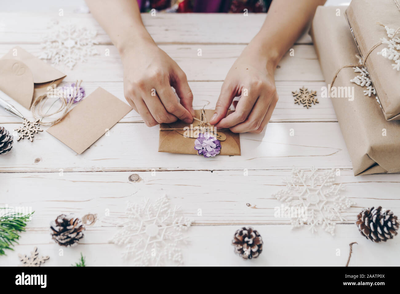 In der Nähe der Hände, die Verpackung Geschenkbox und Weihnachten Karte auf Holztisch mit Weihnachten Dekoration. Stockfoto