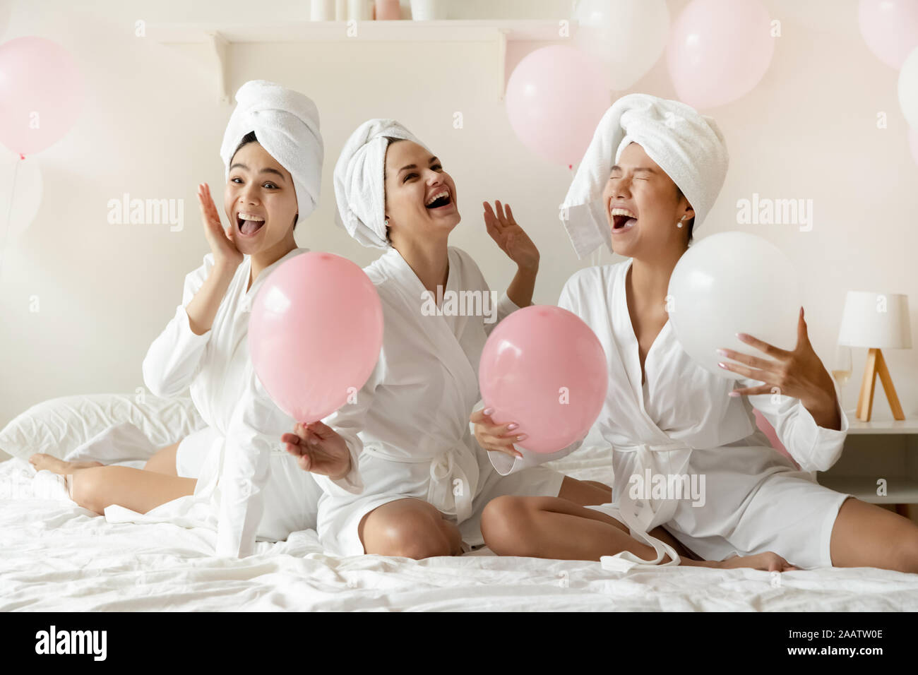 Aufgeregt multiethnischen junge Damen sitzen auf dem Bett mit rosa Ballons Stockfoto