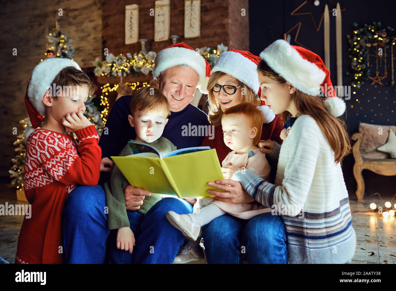 Großeltern, die ein Buch lesen mit einem Kind im Zimmer mit Baum am Weihnachtstag. Stockfoto