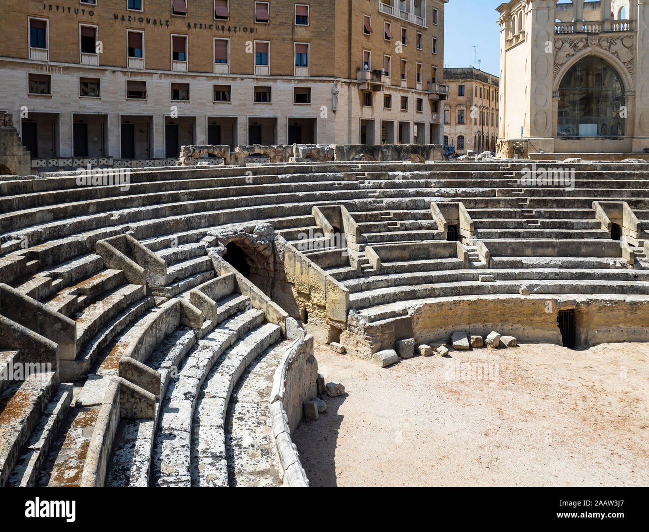 Römische Amphitheater gegen Gebäude in der Altstadt während der sonnigen Tag, Lecce, Italien Stockfoto