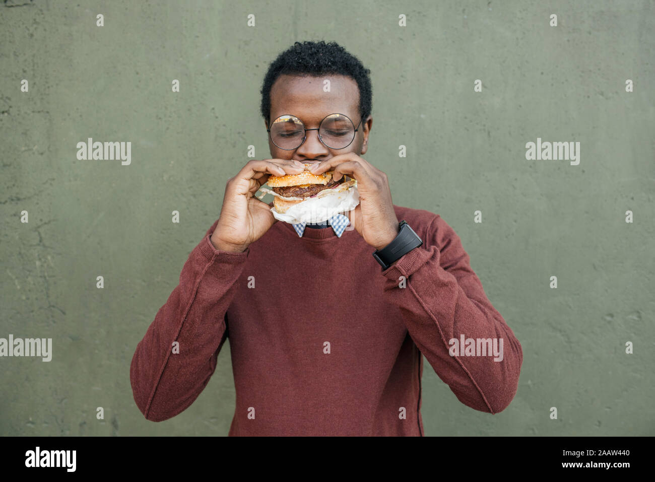 Junger Mann essen Cheeseburger, mit geschlossenen Augen Stockfoto