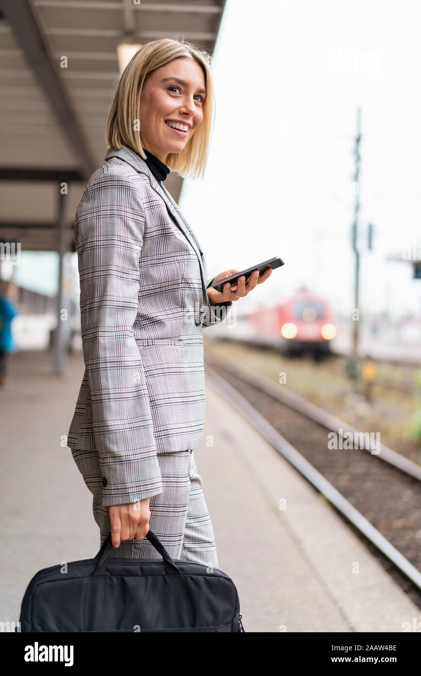 Lächelnden jungen Geschäftsfrau mit Mobiltelefon am Bahnhof Stockfoto