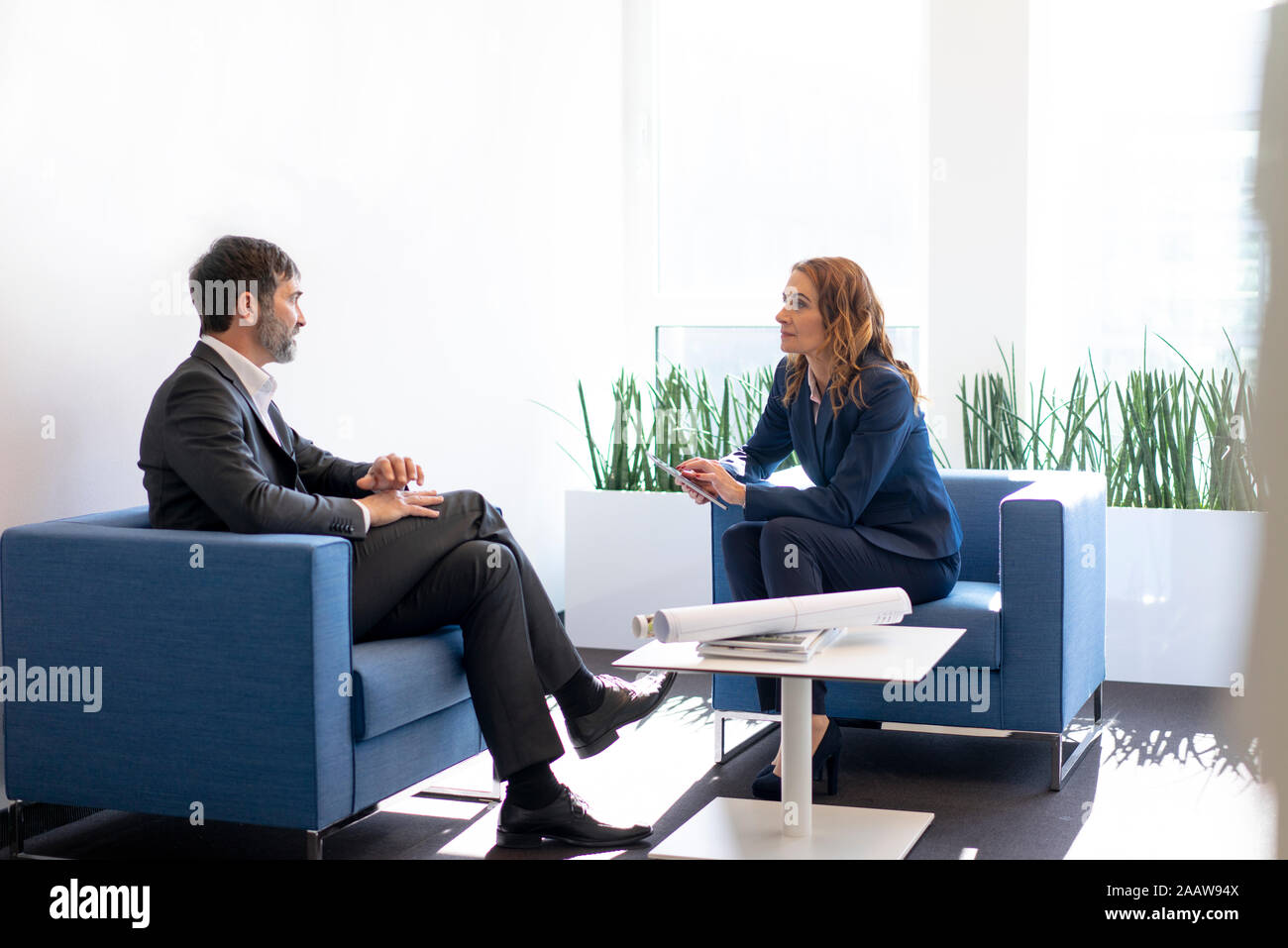 Business-frau und Geschäftsmann in den Sesseln sitzen im Büro sprechen Stockfoto