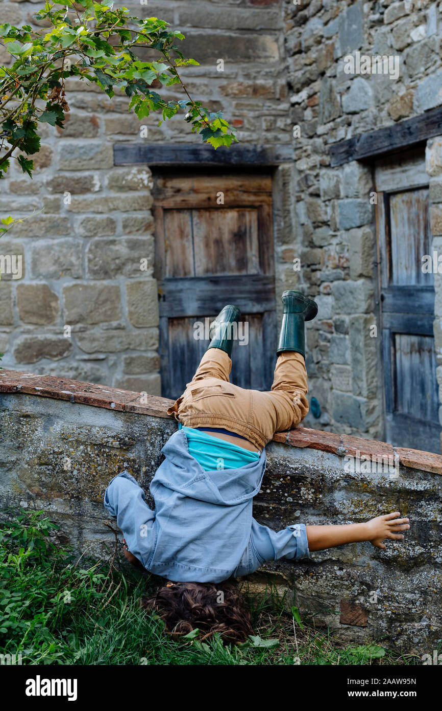 Verspielte Junge tut ein Kopfstand zu einem rustikalen Bauernhaus Stockfoto