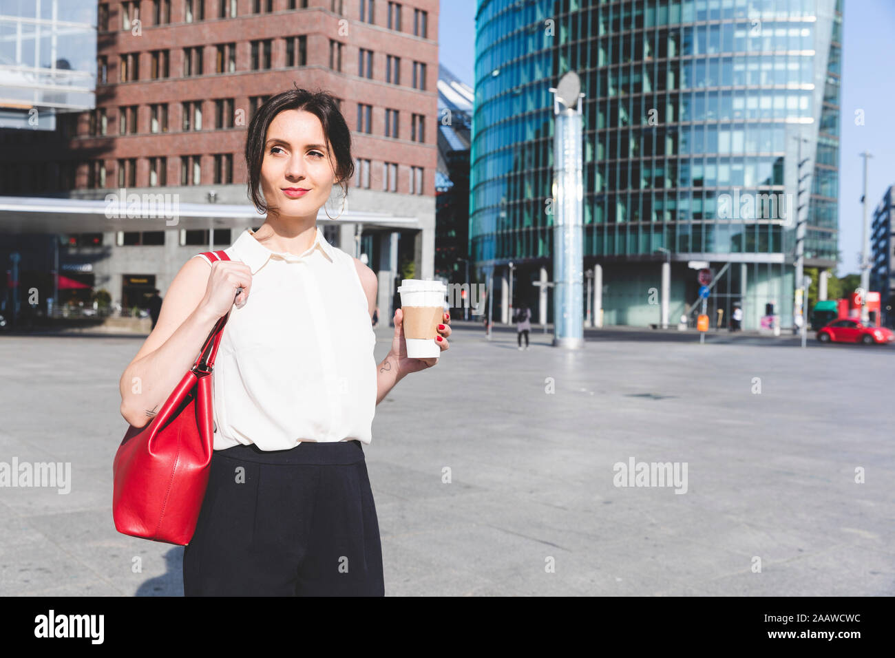 Junge Geschäftsfrau mit Kaffee zum Mitnehmen in der Stadt unterwegs, Berlin, Deutschland Stockfoto