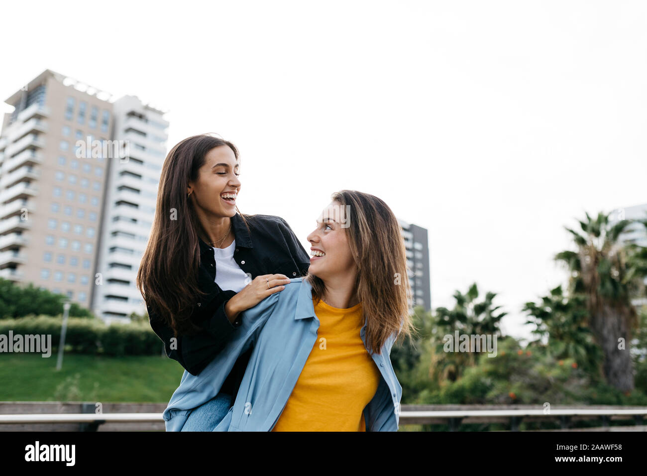 Lachende Frau, die ihre beste Freundin Huckepack in einem Park Stockfoto