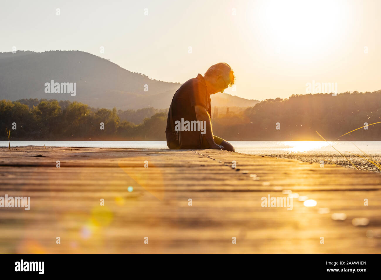Älterer Mann sitzt auf einem Holzsteg und blickte nach unten, gegen die Sonne Stockfoto