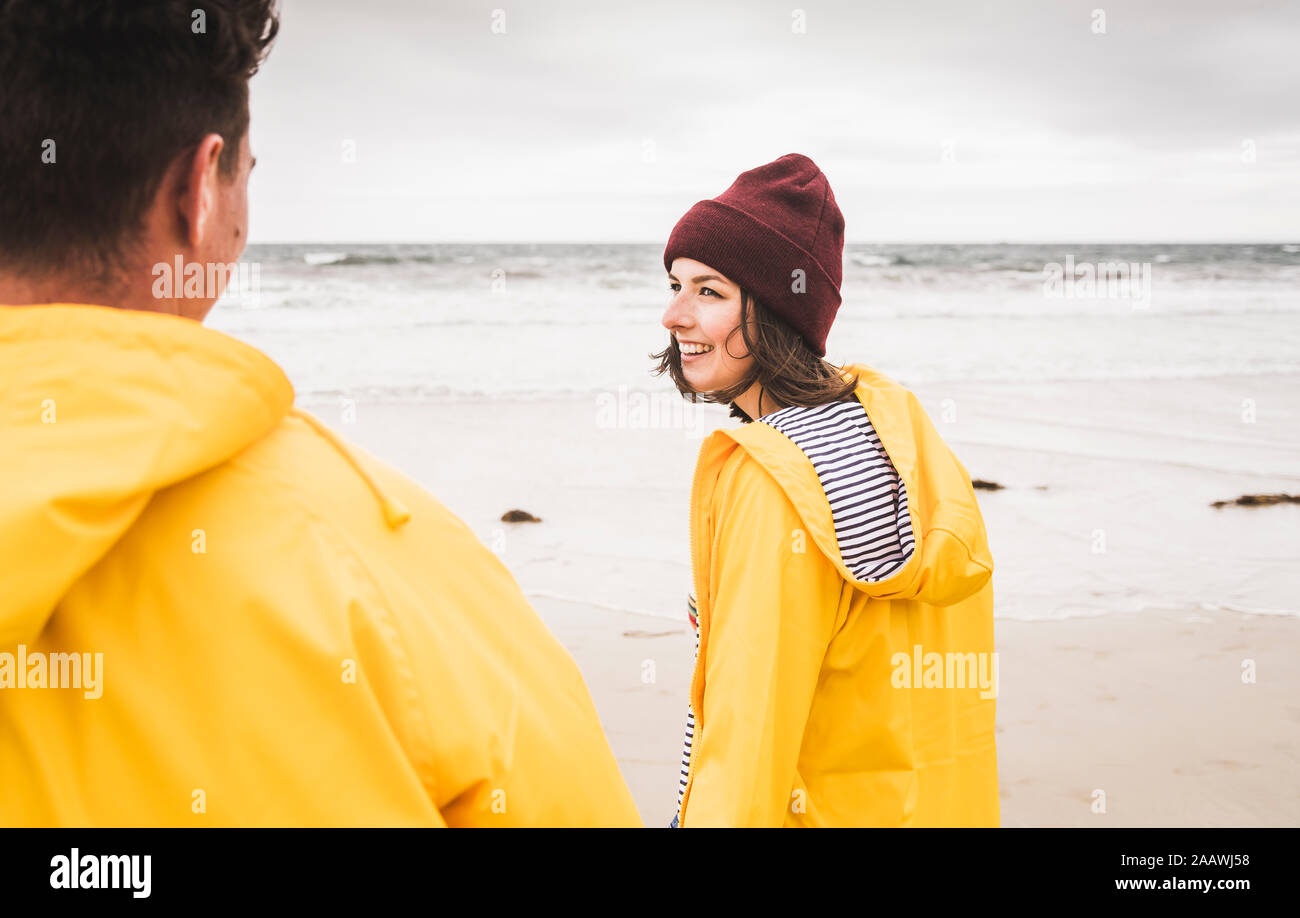 Junge Frau tragen gelbe Regenjacken und zu Fuß am Strand entlang, Bretagne, Frankreich Stockfoto