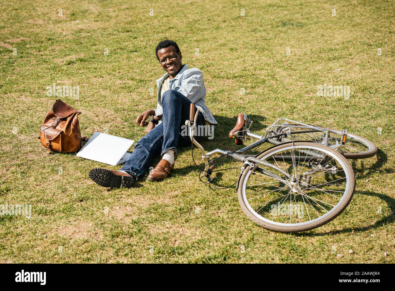 Junger Mann mit alptop und Fahrrad, liegend auf Gras Stockfoto
