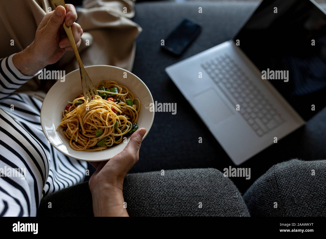 Reife Frau mit Laptop Essen hausgemachte Pasta auf der Couch zu Hause Stockfoto
