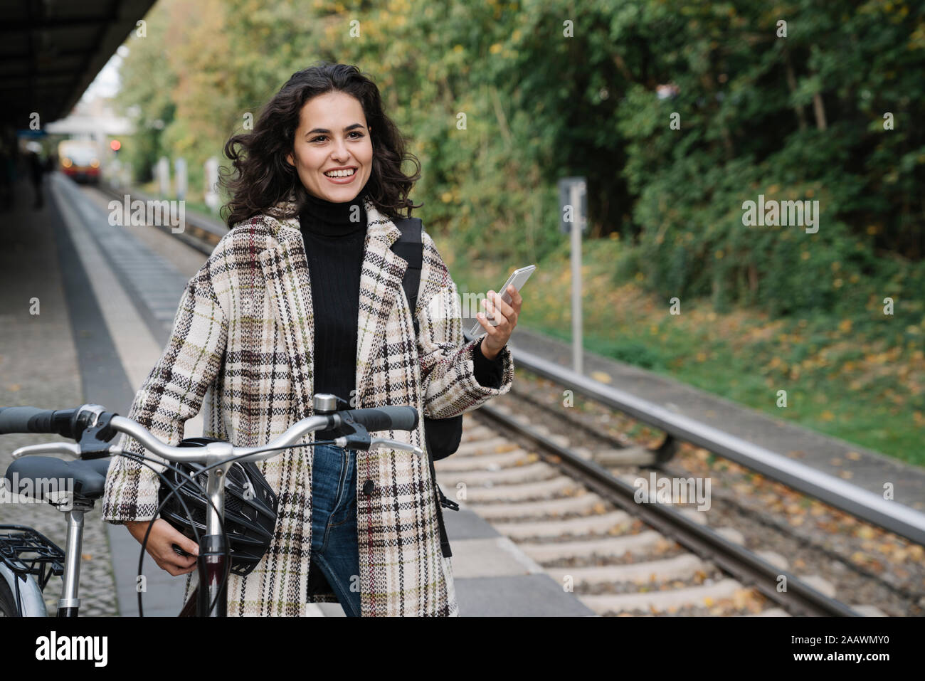 Lächelnde Frau mit Fahrrad und Handy auf einem U-Bahnhof Plattform, Berlin, Deutschland Stockfoto
