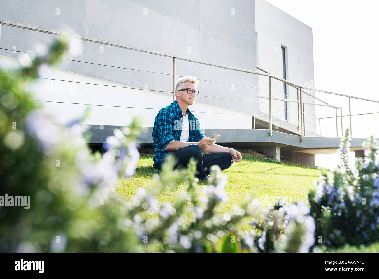 Legerer Mann außerhalb seines modernen Home holding Smartphone Stockfoto