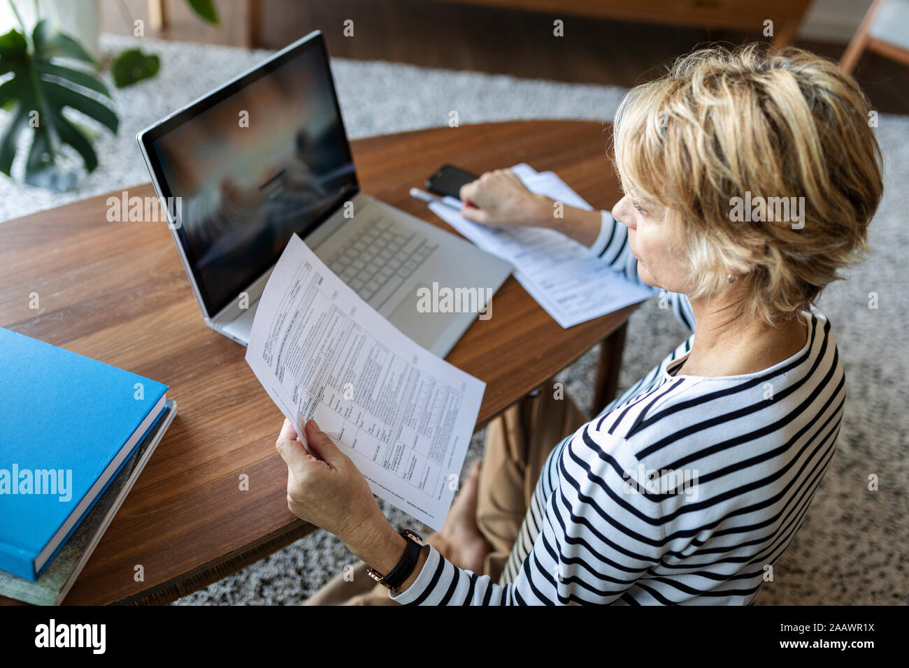 Reife Frau mit Dokumenten über Laptop zu Hause Stockfoto
