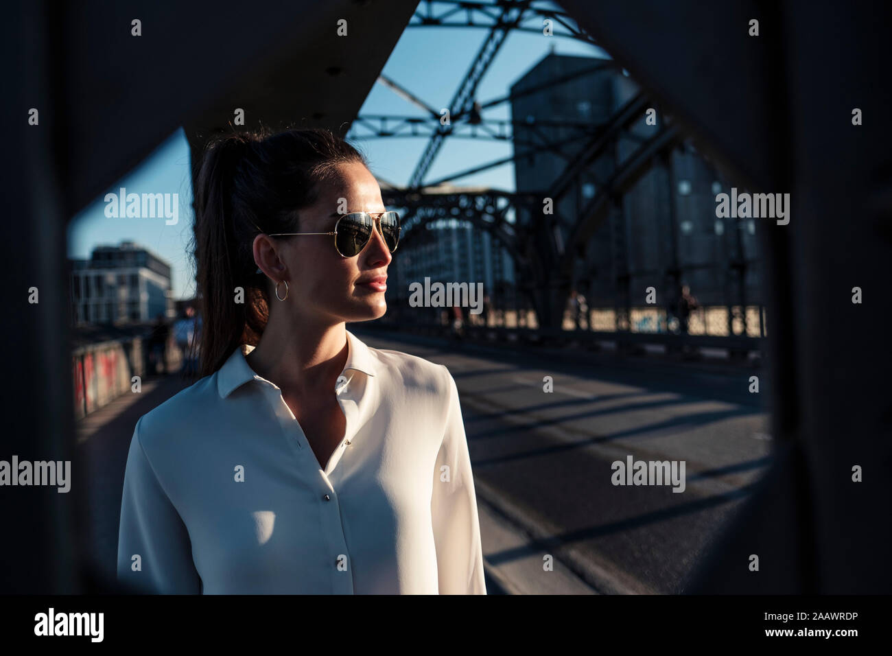 Junge Frau auf einer Brücke, die in der nächtlichen Beleuchtung durch Brückenpfeiler gesehen Stockfoto