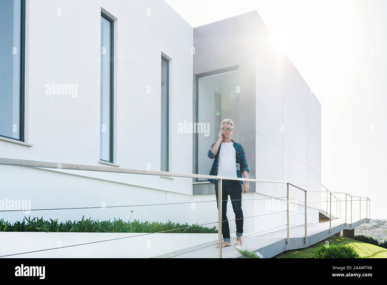 Legerer Mann außerhalb seines modernen Home Unterhaltung am Telefon Stockfoto