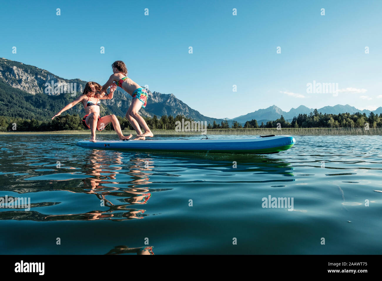 Schwestern kämpfen auf paddle Board, Lake Bannwaldsee, Deutschland Stockfoto