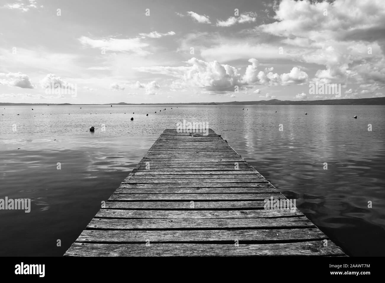 Hölzerne Anlegesteg für Boote vor blauem Himmel mit einigen Wolken. Bojen. Hügeln im Hintergrund. Bolsena See, Italien. Stockfoto