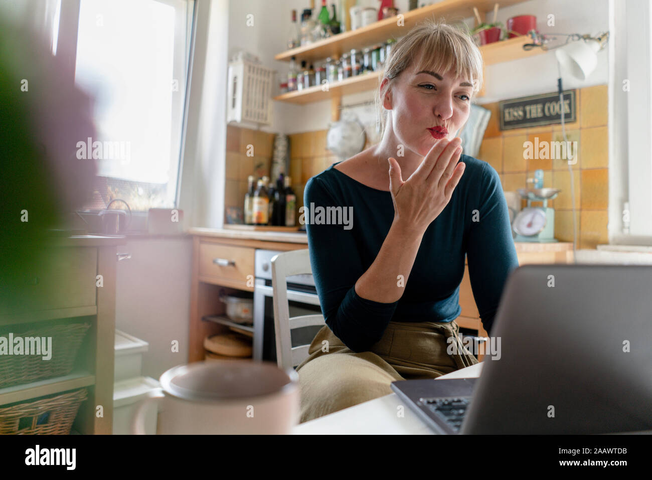 Porträt der jungen Frau mit Laptop in der Küche, bläst einen Kuss Stockfoto