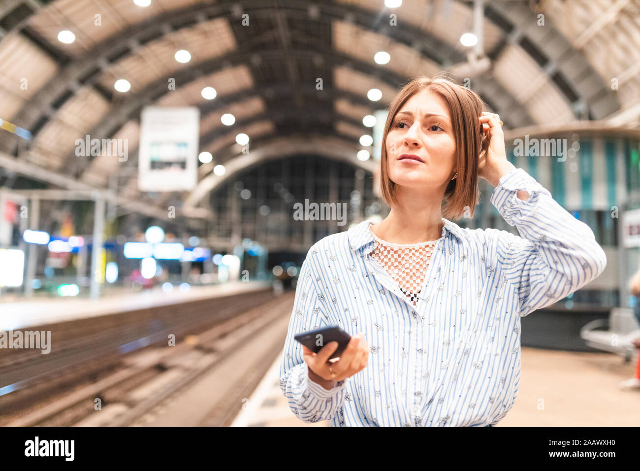 Junge unglückliche Frau mit Smartphone am Bahnhof Stockfoto