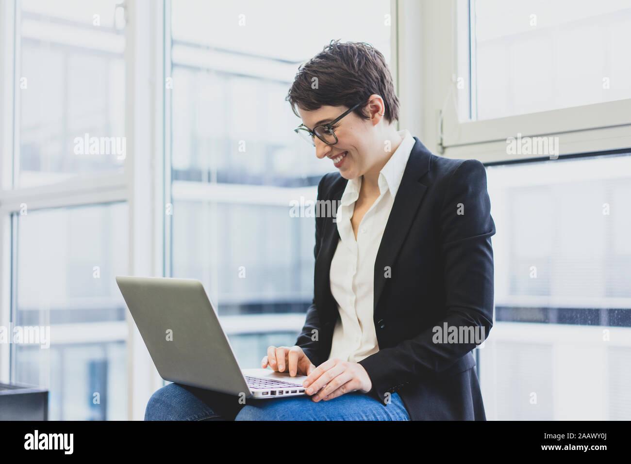 Lächelnden jungen Geschäftsfrau mit Laptop am Fenster Stockfoto