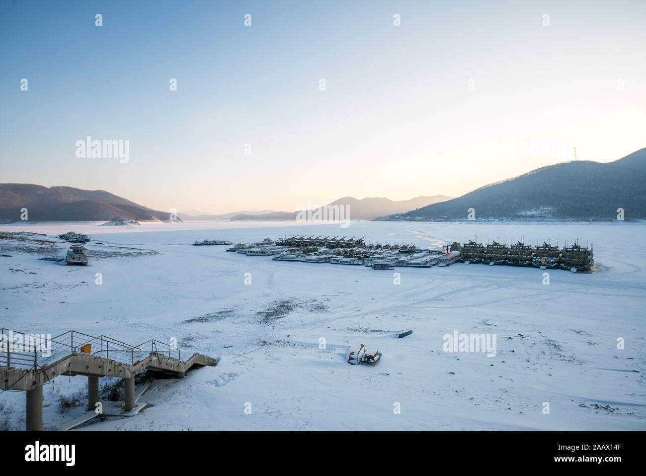 Winterlandschaft von Sonnenuntergang am See Songhua gegen Schnee Berge und zugefrorenen See mit Nebel auf dem See Oberfläche, Provinz Jilin, China Stockfoto