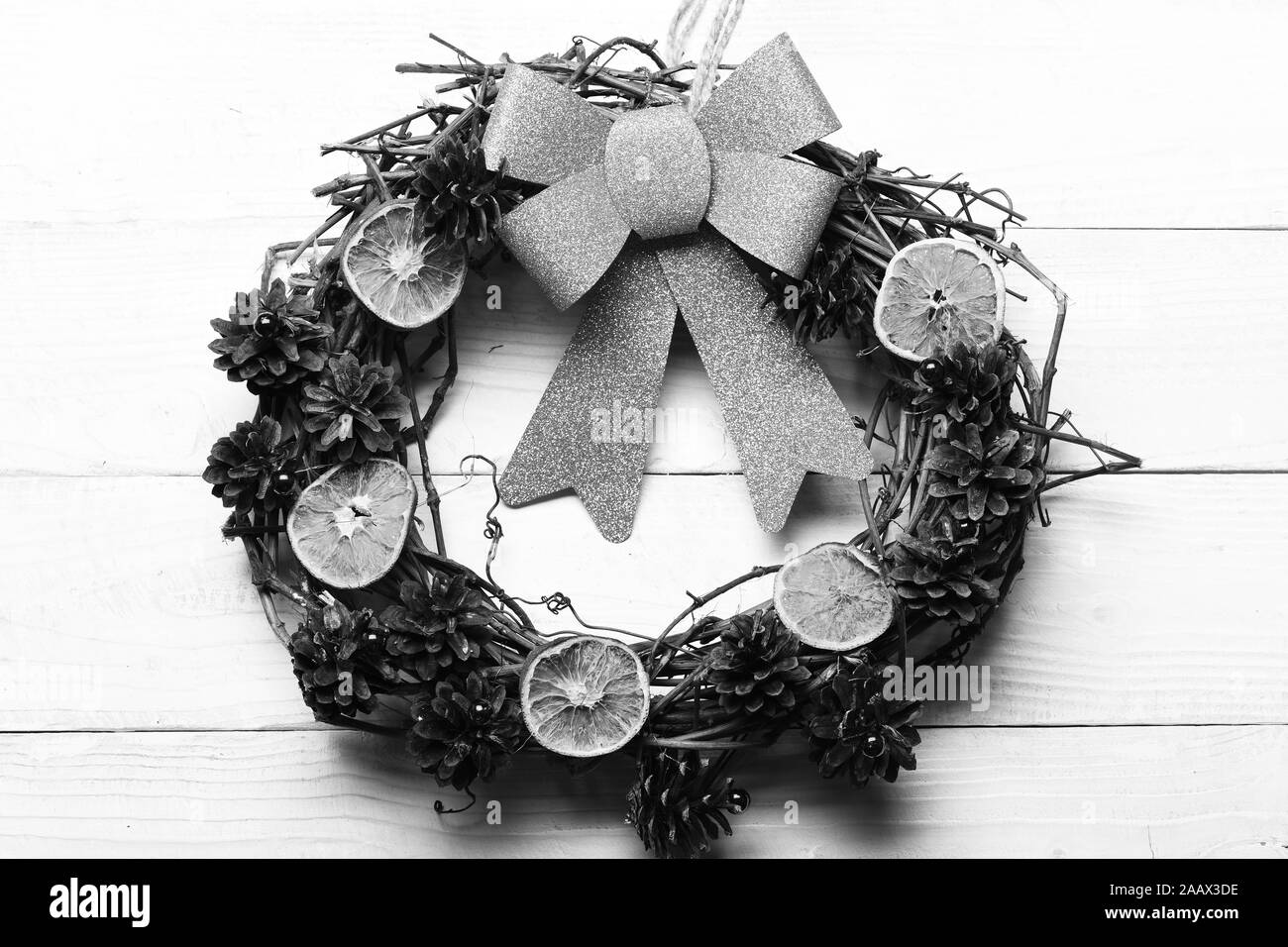 Kranz aus Traubenmost Zweige mit trockenen Citrus Schichten und Tannenbaum Kegel. Weihnachtsdekoration mit organischen Spielzeug. Weihnachtsdekor Konzept. Eco Kranz und großen goldenen Bogen auf weißem Holz- Hintergrund Stockfoto