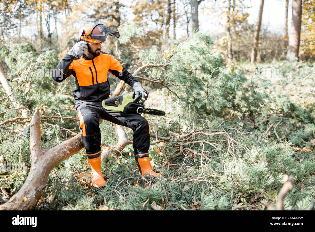 Porträt eines professionellen lumberman in schützende Arbeitskleidung sitzen mit einer Kettensäge auf der gefällten Baumes, ruht nach der harten Arbeit im Wald Stockfoto