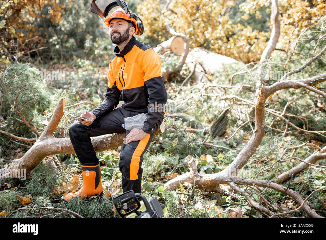 Porträt eines professionellen lumberman in schützende Arbeitskleidung sitzen auf den gefällten Baum beim Ausruhen nach der harten Arbeit im Wald Stockfoto