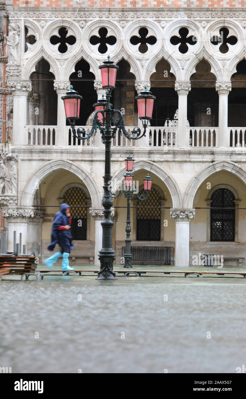 Straßenlaterne und der Dogenpalast in Venedig während hige Tide und Person Wanderungen auf dem Gehweg über dem Meer Stockfoto