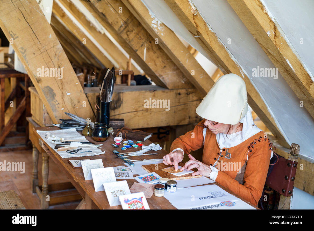 Mittelalterliche Geschichte. Nahaufnahme von einer reifen Frau in Kostümen mit einem Blatt Gold Leaf eine beleuchtete Buchstaben zu Papier zu vergolden gekleidet. Stockfoto