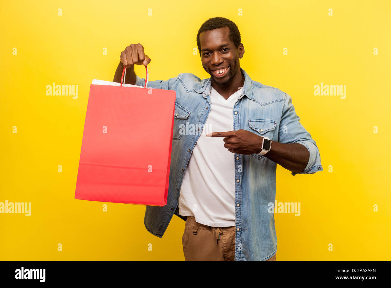 Portrait von leidenschaftlich gerne männliche Käufer mit attraktiven toothy Lächeln legere Kleidung an Einkaufstaschen, Denim, schaut zufrieden. indo Stockfoto