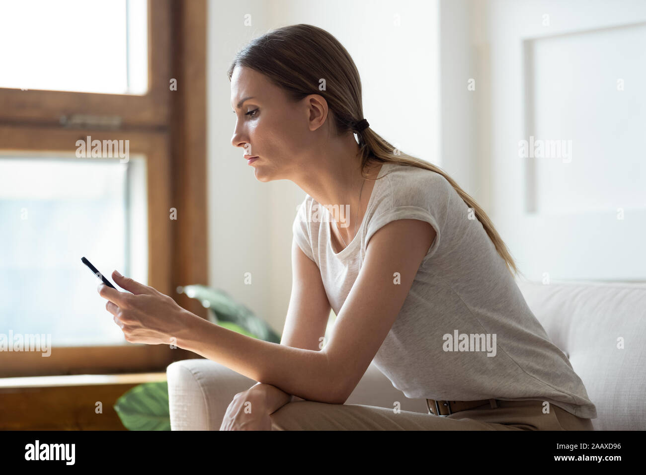Nachdenkliche junge Frau am Handy Bildschirm schaut. Stockfoto