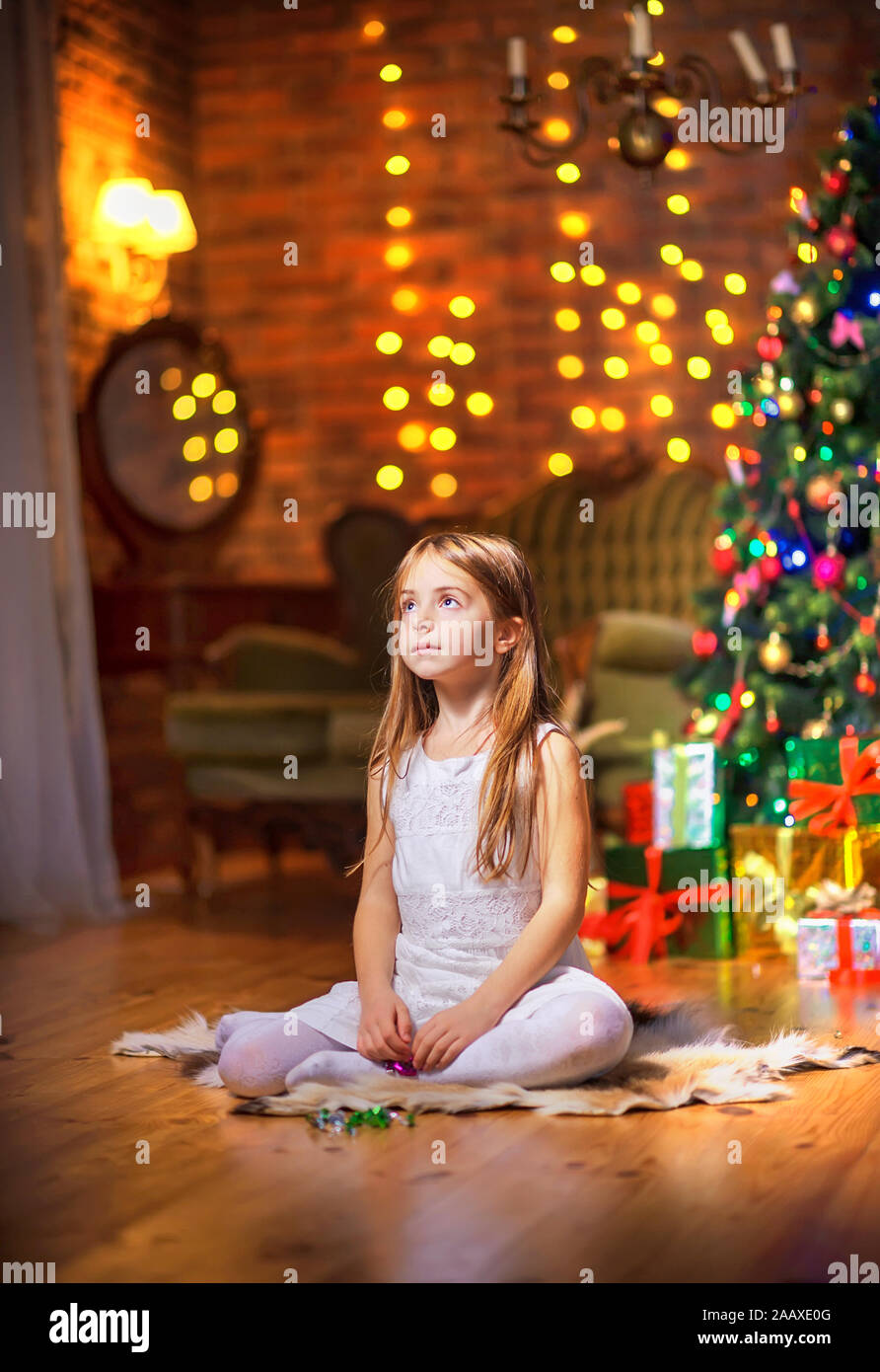Süße kleine Mädchen sitzt auf dem Boden am Abend im Zimmer in der Nähe der festlichen Weihnachtsbaum und Träume. Weihnachten und neues Jahr. Stockfoto