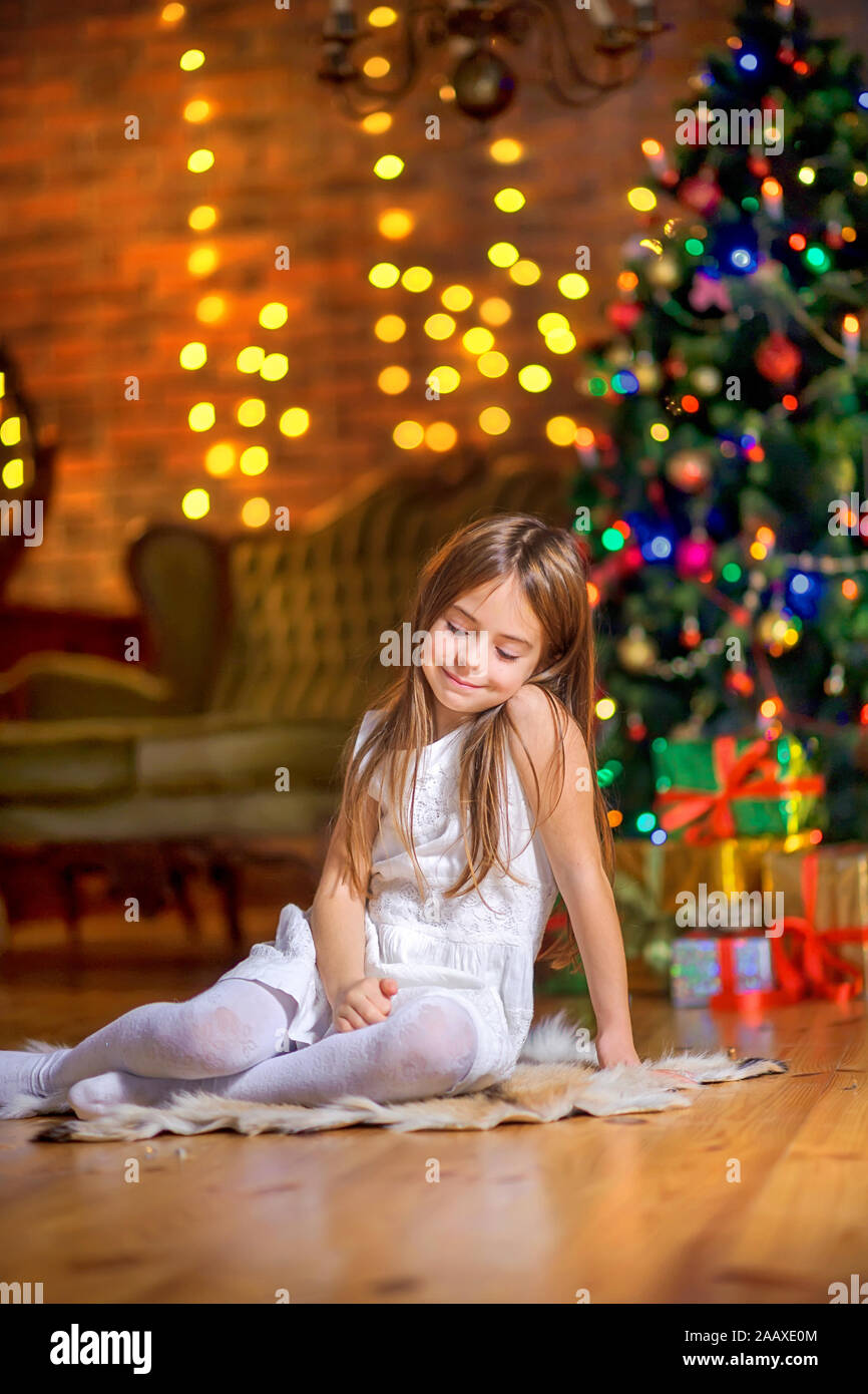 Süße kleine Mädchen sitzt auf dem Boden am Abend im Zimmer in der Nähe der festlichen Weihnachtsbaum und Träume. Weihnachten und neues Jahr. Stockfoto