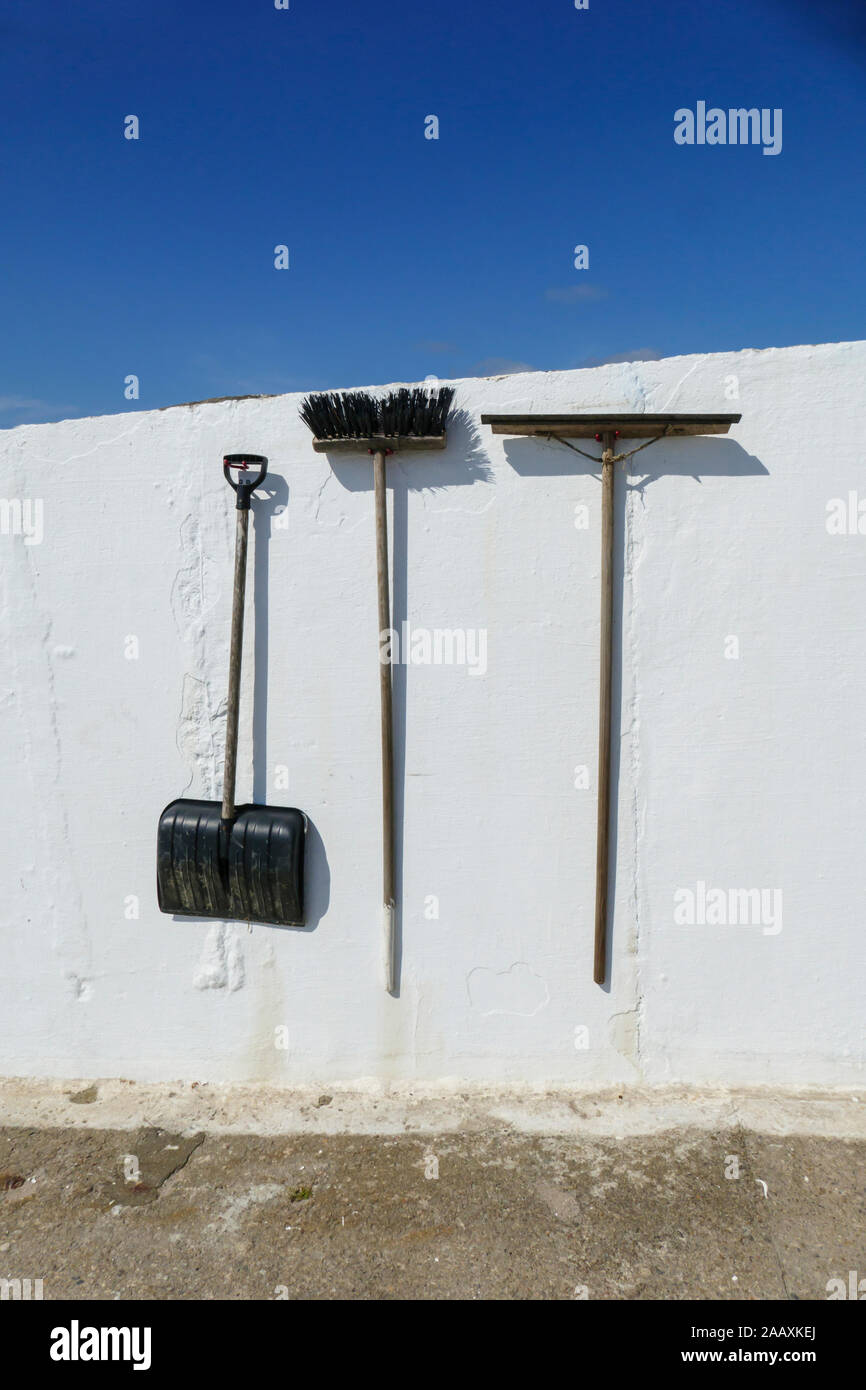 Schnaufel, Besen und Schneeschippe, Wasserabstreifer verhängen Eine einer weißen Wand Stockfoto