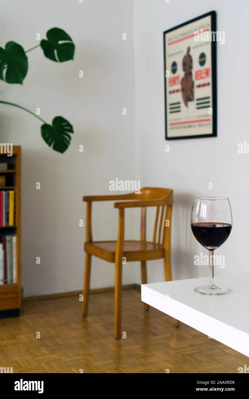 Home Interior mit einem Glas Rotwein auf dem weißen Tisch, verschwommenen Hintergrund mit hölzernen Stuhl im Zimmer Ecke Stockfoto