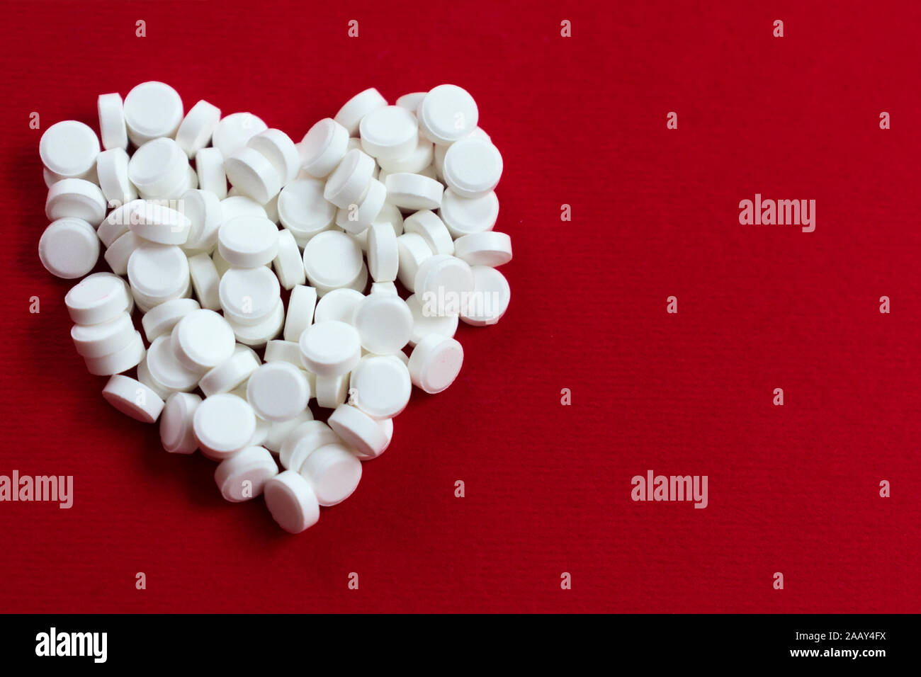 Ein Herz aus kleinen weißen Pillen auf einem roten Hintergrund. Das Konzept der Herzkrankheit. Stockfoto
