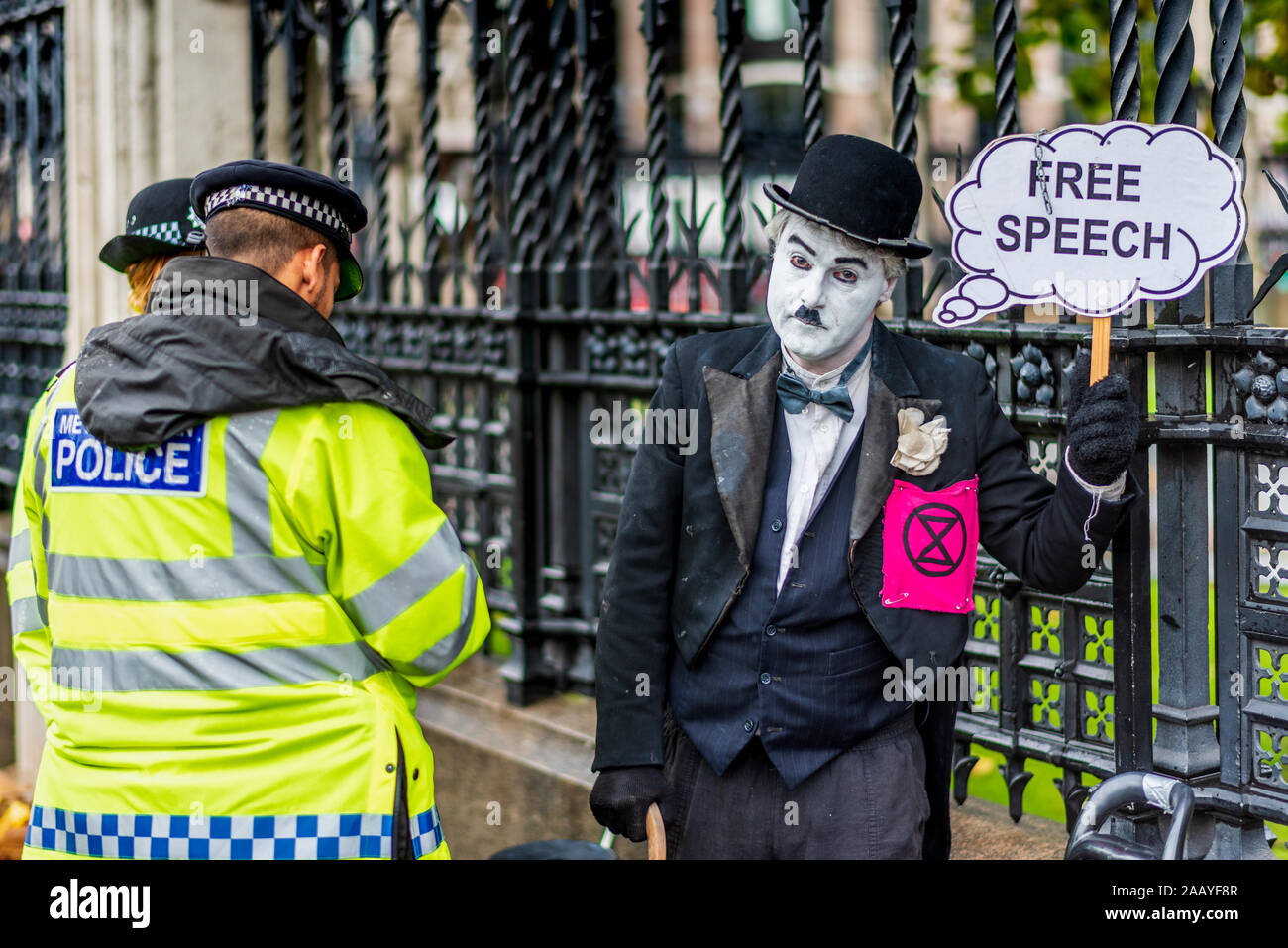 Freie Rede Parlament des Vereinigten Königreichs. Polizei Frage ein Aussterben Rebellion Demonstrant in Chaplin Art Kleidung außerhalb der Häuser des Parlaments London gekleidet. Stockfoto