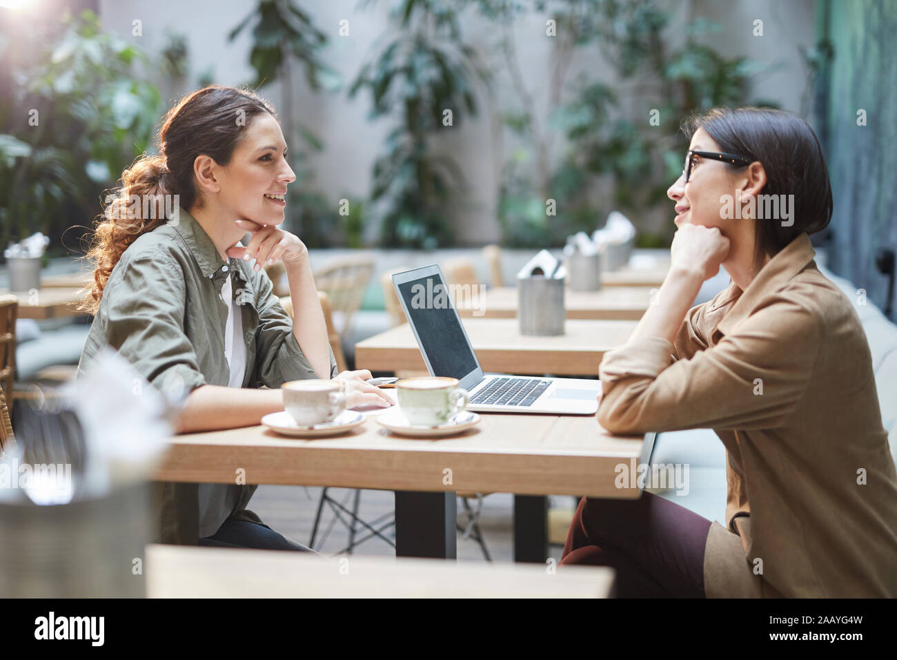 Seitenansicht Portrait von zwei moderne junge Frauen am Tisch sitzen im Café, beim Besprechen des Unternehmens während der Sitzung auf der Terrasse im Freien Platz, kopieren Stockfoto