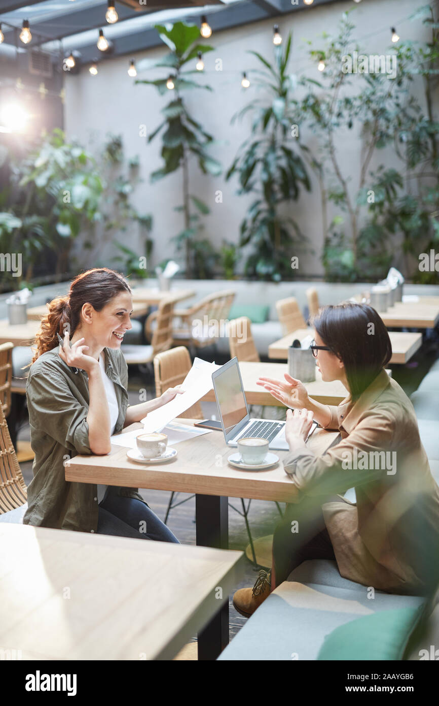 Hohen winkel Portrait von zwei moderne junge Frauen am Tisch sitzen in Designer Cafe und freundlich lächelnd, beim Besprechen des Business, Platz kopieren Stockfoto