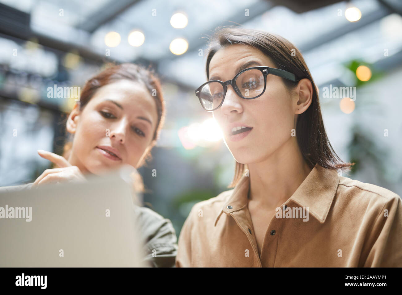 Low Angle Porträt des zeitgenössischen junge Frau mit Laptop im Cafe während der Arbeit am Projekt mit Kollegen Stockfoto