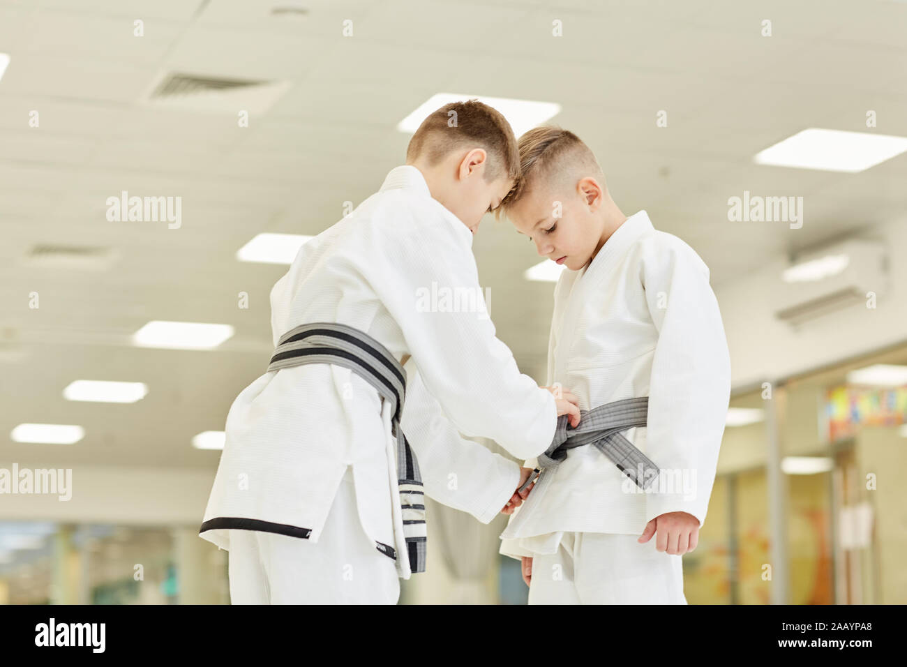 Junge in Kimono stehen und Helfen, um den Riemen zu seinem Freund zu binden vor dem Training im Karate in der Turnhalle Stockfoto