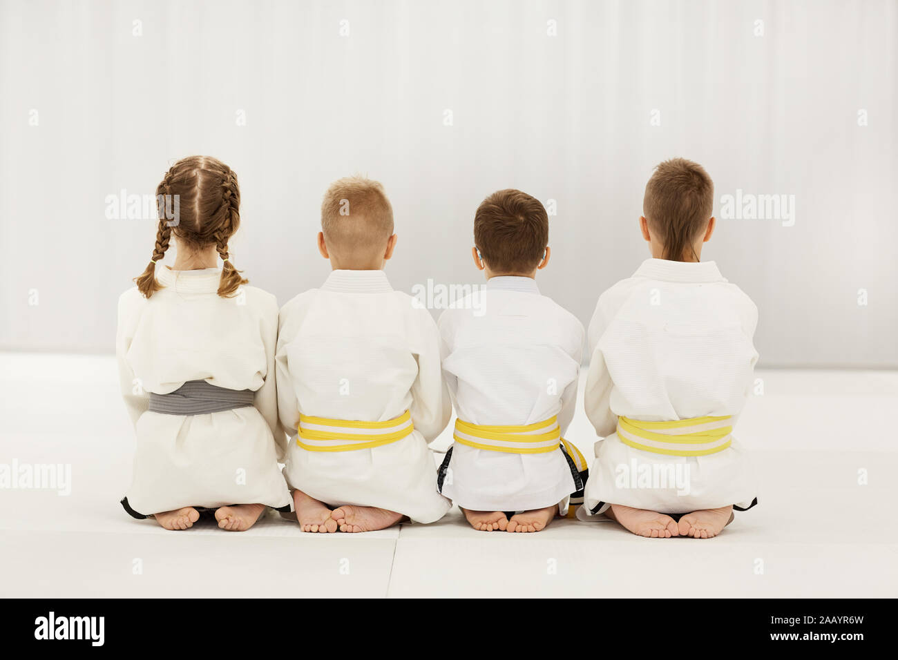 Ansicht der Rückseite des barfüßigen Kinder in weißen Kimono auf dem Fußboden sitzen zusammen in einer Zeile Stockfoto