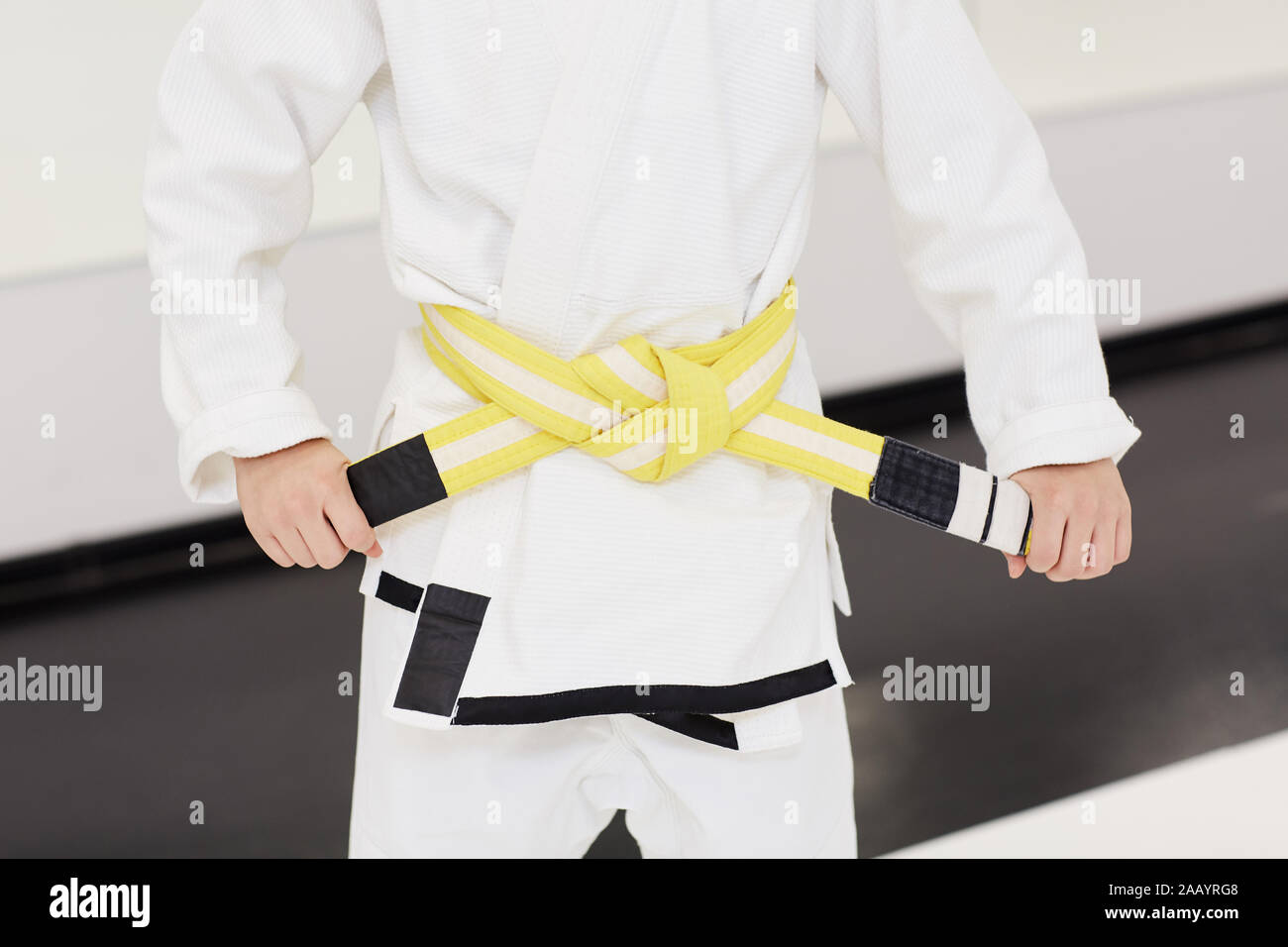 In der Nähe des kleinen Jungen im weissen Kimono und tieing den gelben Gürtel auf seine Taille vor dem Training im Karate Stockfoto