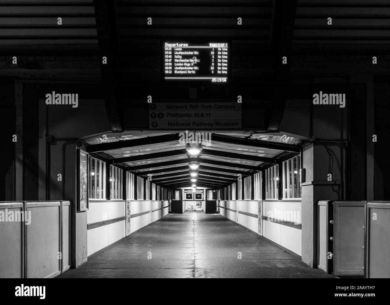 York Bahnhof bei Nacht. Eine getunnelte Fußgängerbrücke über den Bahnsteigen leuchtet, gegen den dunklen Eingang. Einem elektronischen schwarzen Brett ist ein Stockfoto