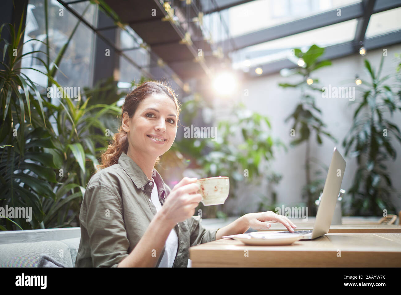 Portrait von lächelnden jungen Frau mit Kamera beim Arbeiten mit Laptop im Café im Freien Terrasse und genießen Kaffee, Kopie Raum Stockfoto