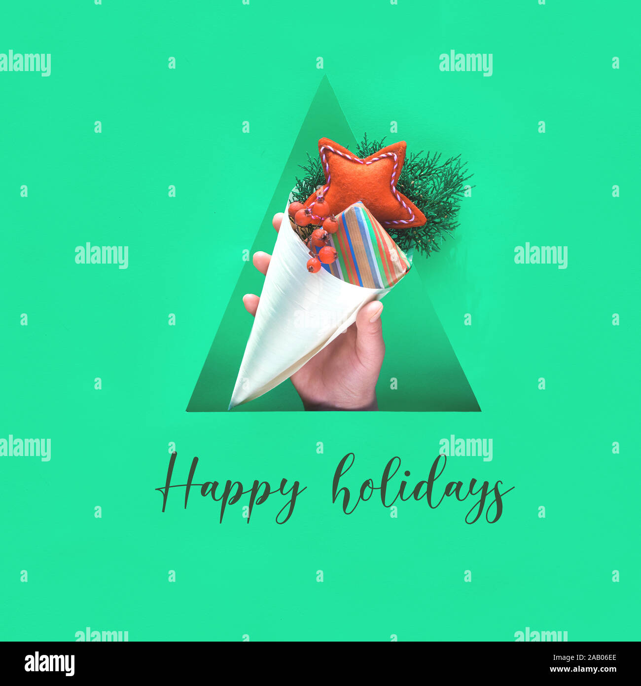 Happy Holidays Text. Hand mit natürlichen Dekorationen, Geschenkbox im Handwerk Papier und weichen Filz handgefertigter roter Stern in Sperrholz Kegel in dreieckigen Papier Loch. Stockfoto