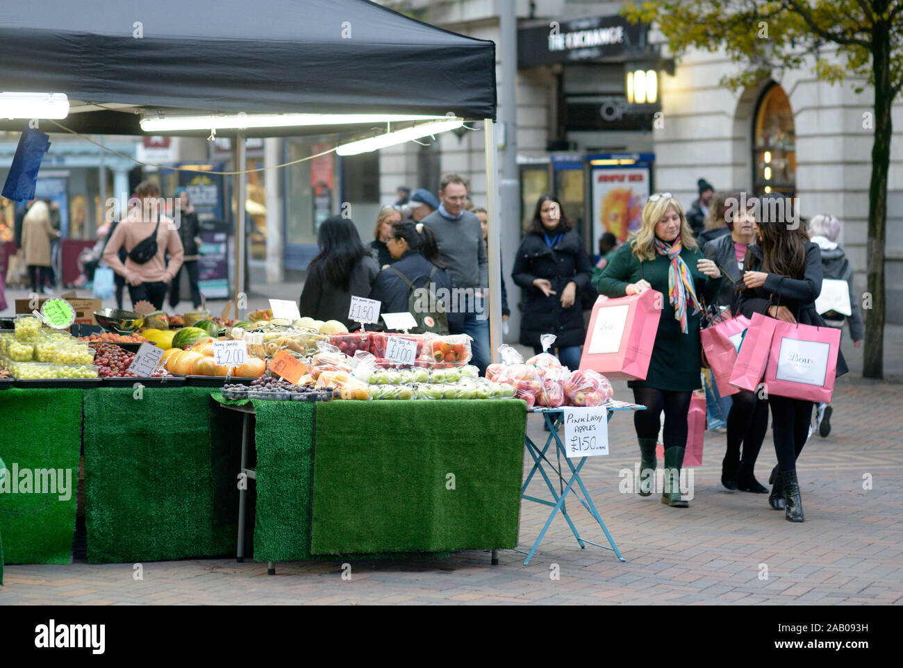 Frauen mit rosa Einkaufstaschen, vorbei an einem Obststand, in Nottingham. Stockfoto