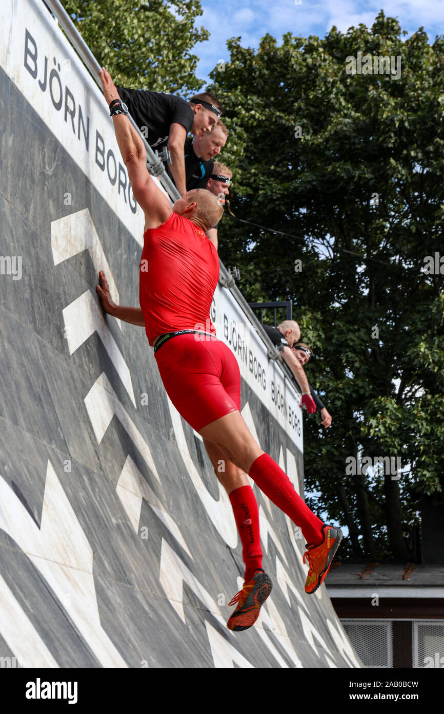 Mann in roten Outfit, die versuchen, ein Hindernis, obwohl Viking Race 2019 in Helsinki, Finnland zu erobern. Stockfoto