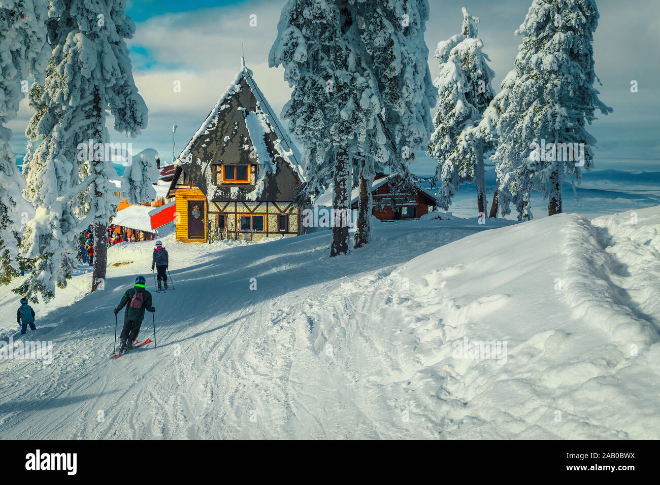 Winter Skigebiet mit hölzernen Hütten in der Nähe der Skipiste. Schnee bedeckt, Pinien und sportliche Skifahrer auf der Piste, Poiana Brasov Ski Resort, Transylvani Stockfoto